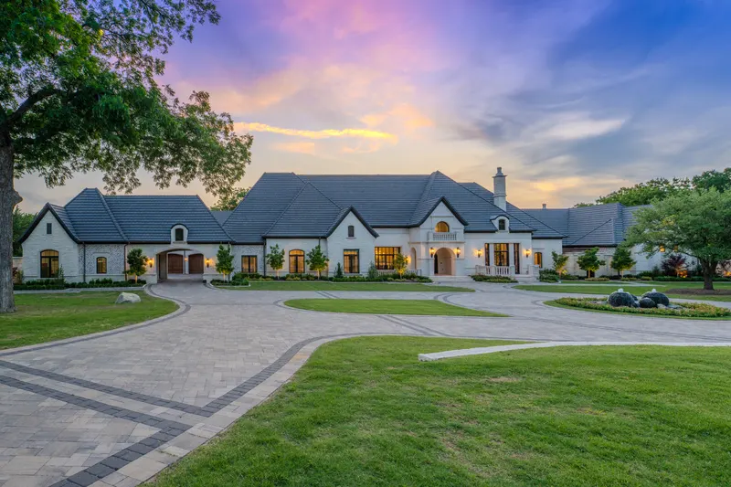 Stone and stucco estate front elevation at sunset with circular paver drive at Bella Terra Estate, Parker TX