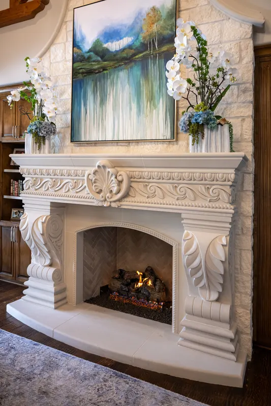 Carved cast stone fireplace with acanthus corbels and lit gas logs