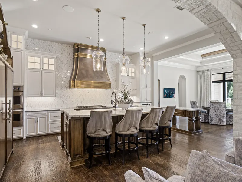 Kitchen island with velvet barstools beneath glass pendants and a brass hood