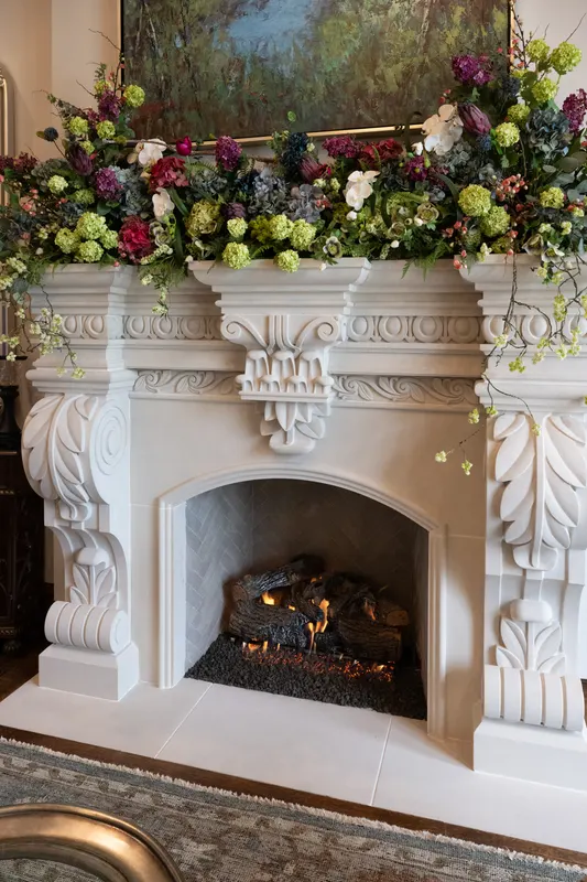 Carved limestone mantel in the library topped with a lush floral arrangement