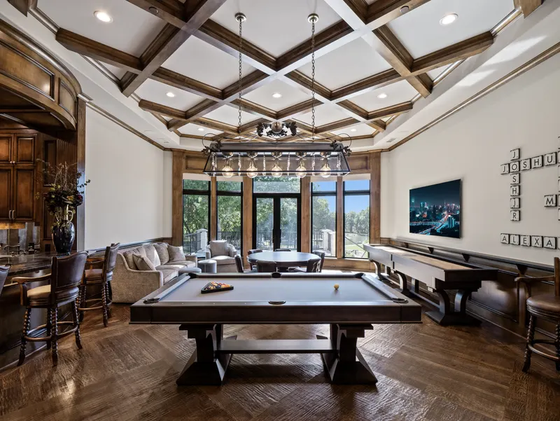 Game room with pool table, shuffleboard and coffered ceiling above a wet bar