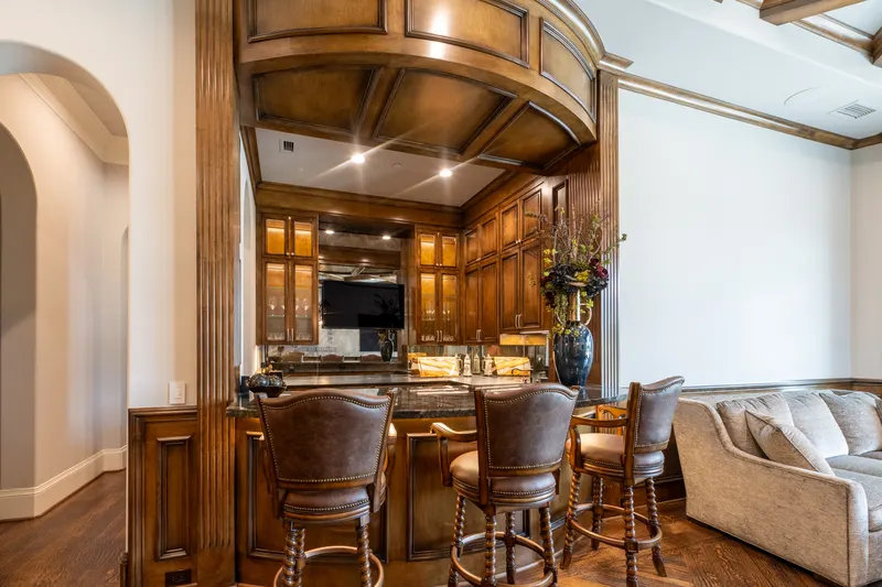 Wet bar with leather barstools, wood cabinetry and a domed coffered soffit