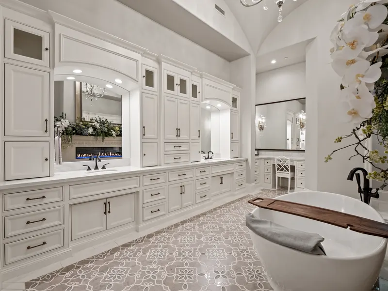 Master bath with a long white vanity, fireplace mirror and freestanding tub