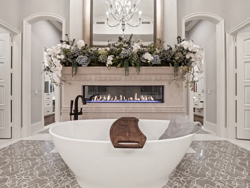 Freestanding soaking tub facing a linear fireplace with floral-topped mantel