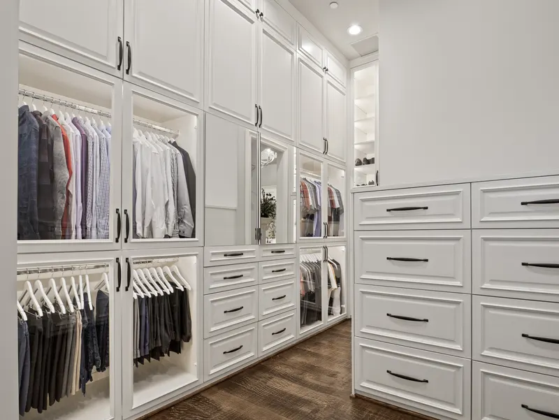 Wraparound master closet with lighted glass-front cabinetry and built-in dresser drawers