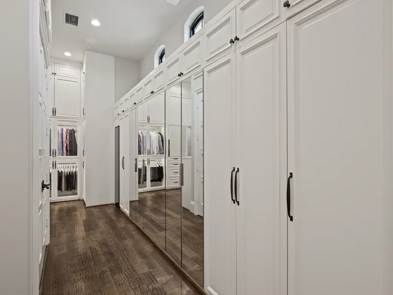 Master closet corridor lined with mirrored wardrobe doors and arched clerestory windows