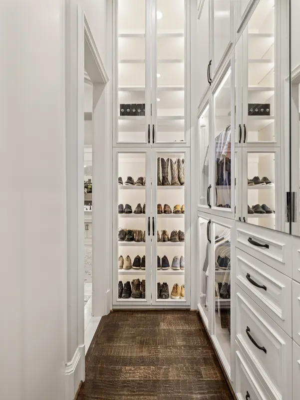 Lighted glass-front shoe cabinetry and watch display in the master closet