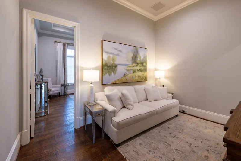 Guest suite sitting room with cream sofa and framed landscape painting over dark oak floors