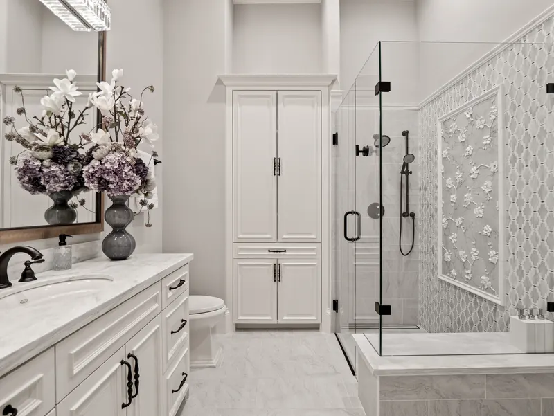 Guest bath with marble vanity, linen tower and glass shower framing a carved floral panel