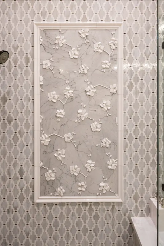 Carved marble orchid relief panel set into arabesque shower tile in a guest bath