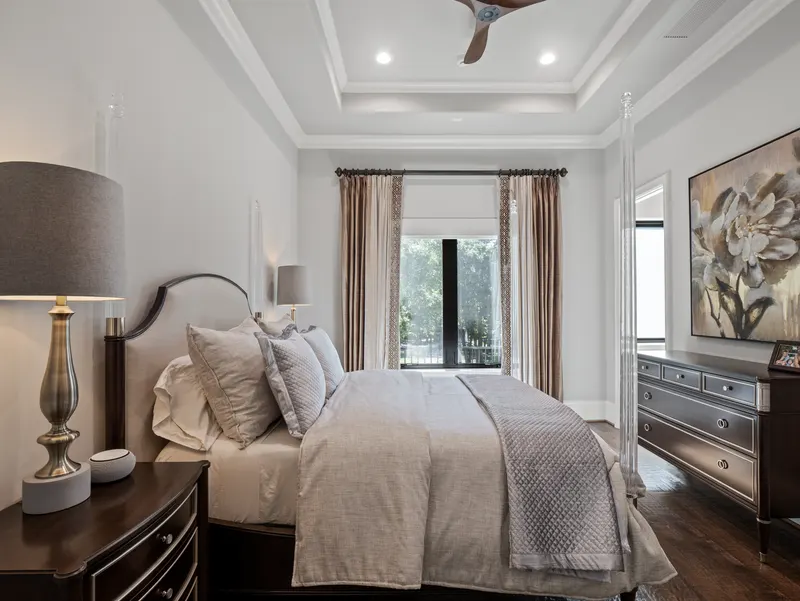 Guest bedroom with acrylic four-poster bed, layered tray ceiling and patio access