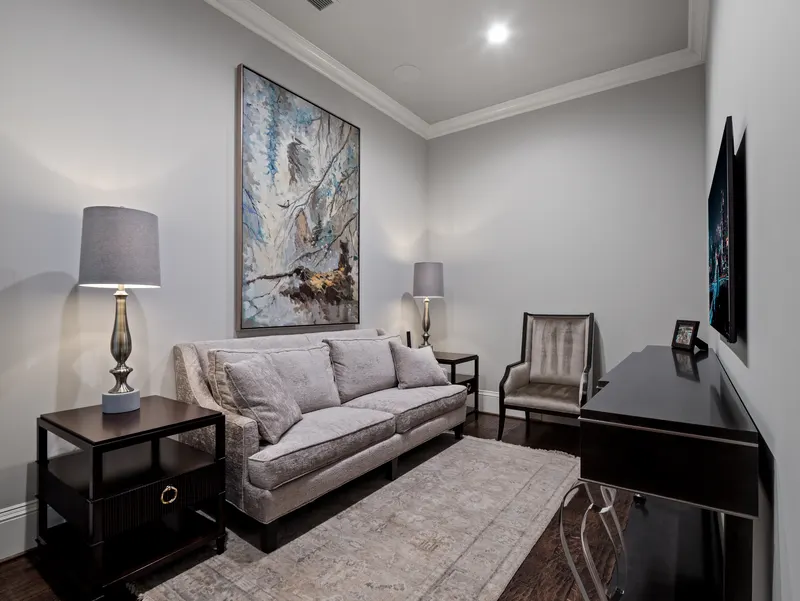 Private sitting room off a guest suite with gray sofa, abstract art and wall-mounted TV