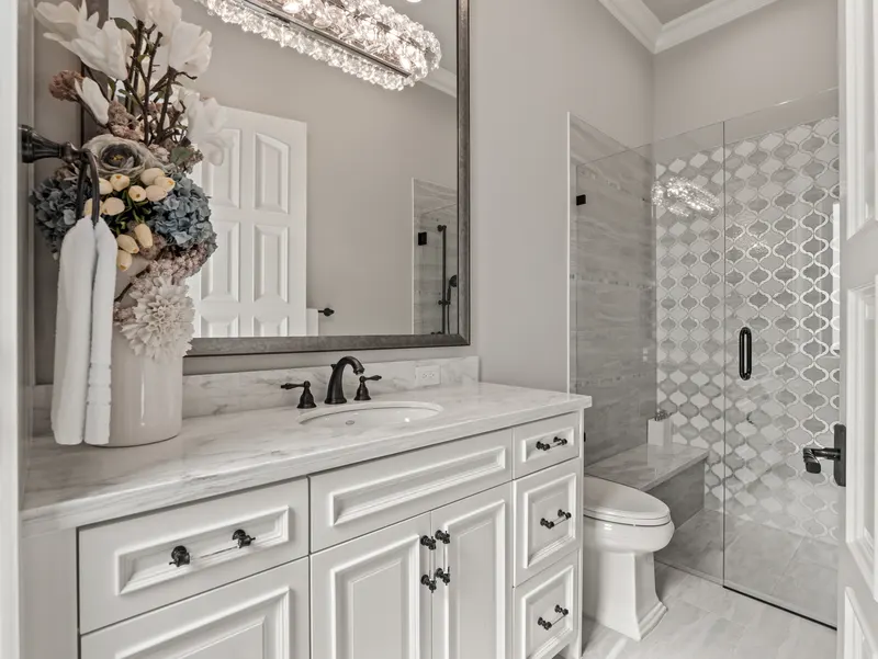 Guest bath with marble-top vanity, crystal light bar and arabesque-tiled glass shower