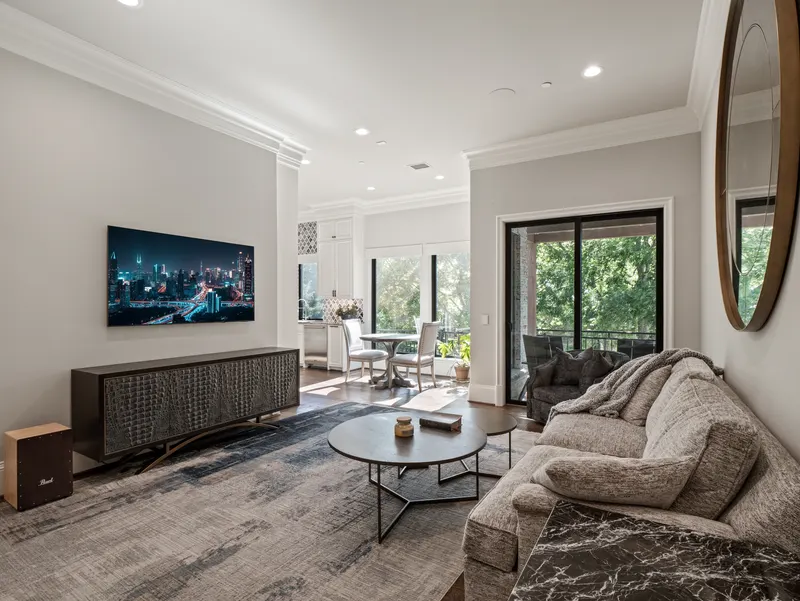 Guest apartment living area with wall TV, sliding glass doors and treetop balcony views