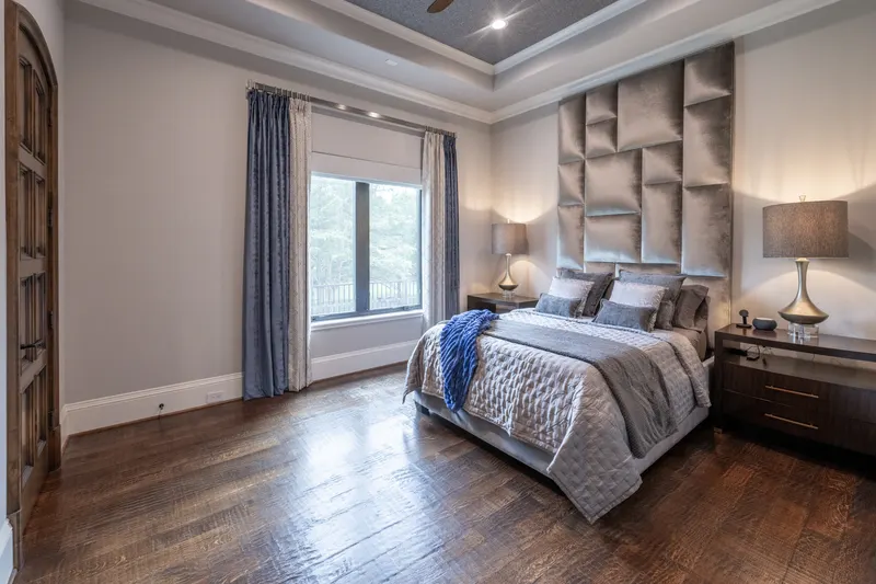 Guest apartment bedroom with padded velvet wall headboard, tray ceiling and arched wood door
