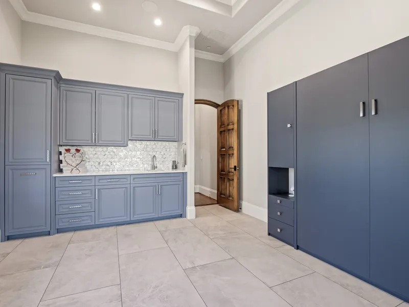 Craft room with slate-blue cabinetry, prep sink and full-height storage by an arched wood door