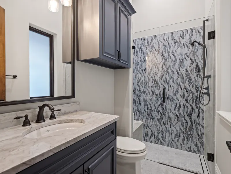 Craft room bath with navy vanity, marble counter and rippled glass-mosaic shower wall