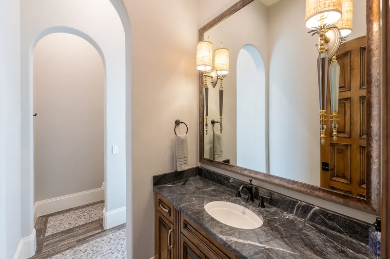 Powder room with charcoal marble vanity, candle sconces and an arched doorway