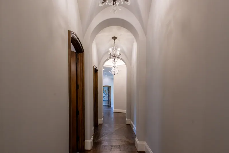 Barrel-vaulted hallway with crystal chandeliers, arched openings and herringbone wood floors
