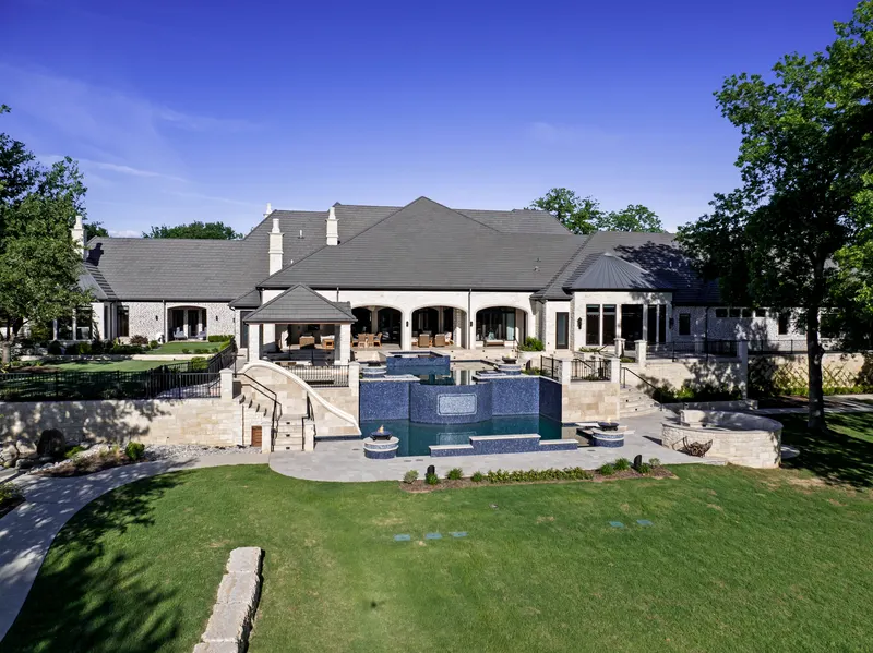 Aerial of the single-story stone rear elevation above the tiered blue-tile pool at Bella Terra Estate, Parker TX