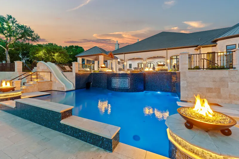 Two-level resort pool glowing at sunset with lit fire bowls and the tall slide at Bella Terra Estate, Parker TX