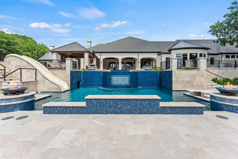 Symmetrical pool view from the travertine deck with waterfall wall and tanning ledge at Bella Terra Estate, Parker TX