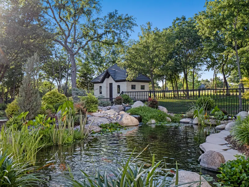 Koi pond edged in boulders and water lilies with the stone garden cottage beyond at Bella Terra Estate, Parker TX