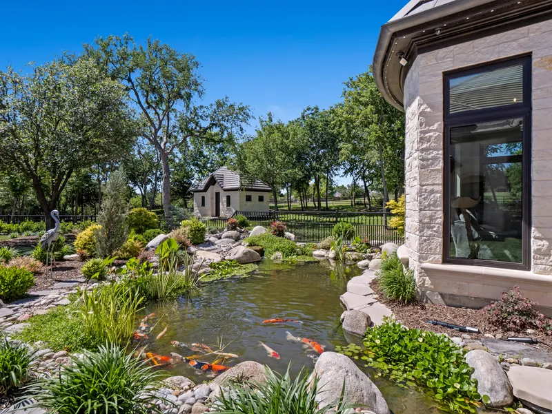Koi pond with heron sculpture and boulder edging beside the stone bay window at Bella Terra Estate, Parker TX