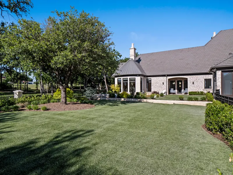Manicured side lawn under a mature oak beside the bay-window wing and arched porch at Bella Terra Estate, Parker TX