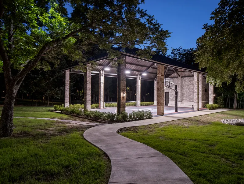 Lighted sport court pavilion glowing at dusk with basketball hoop and winding path at Bella Terra Estate, Parker TX