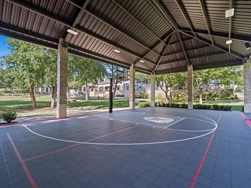 Covered pickleball and basketball court with striped surface under a beamed metal roof