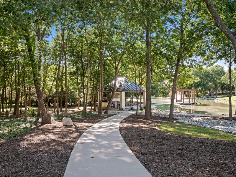 Concrete walking path winding through the woods to a lakeside pavilion at Bella Terra Estate, Parker TX