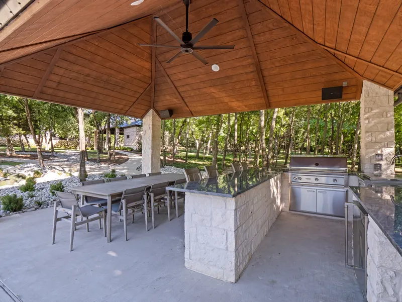 Pavilion outdoor kitchen with granite bar, built-in grill and long dining table under a cedar ceiling