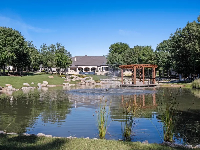 View across the pond to the dock pergola and the covered rear porch at Bella Terra Estate, Parker TX