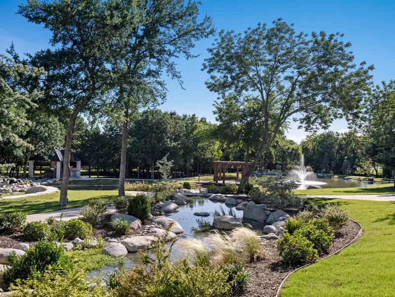 Landscaped stream with ornamental grasses leading to the pond fountain and pergola at Bella Terra Estate, Parker TX