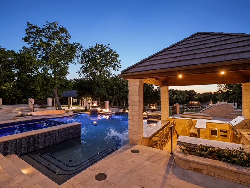 Pool cabana and spa glowing at dusk with fire bowls ringing the water at Bella Terra Estate, Parker TX