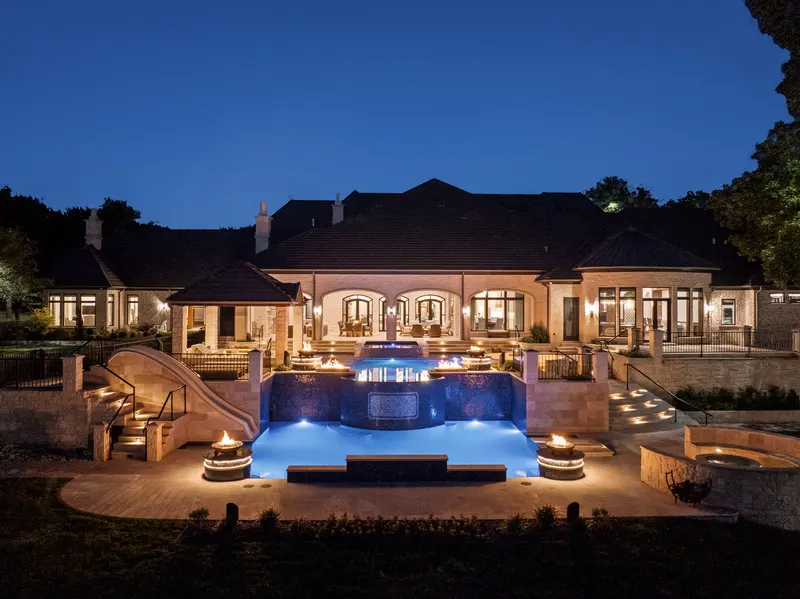Night aerial of the lit rear elevation, blue pool and waterslide at Bella Terra Estate, Parker TX