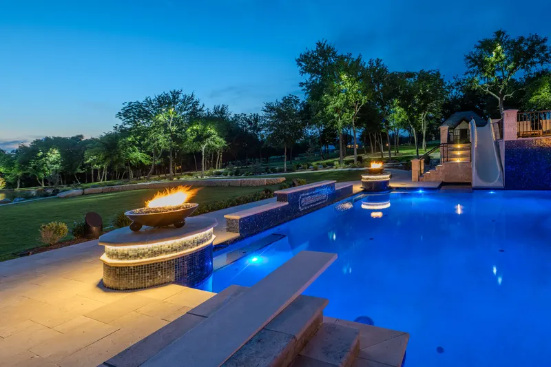 Pool glowing blue after dark with a flaming fire bowl and the waterslide beyond at Bella Terra Estate, Parker TX