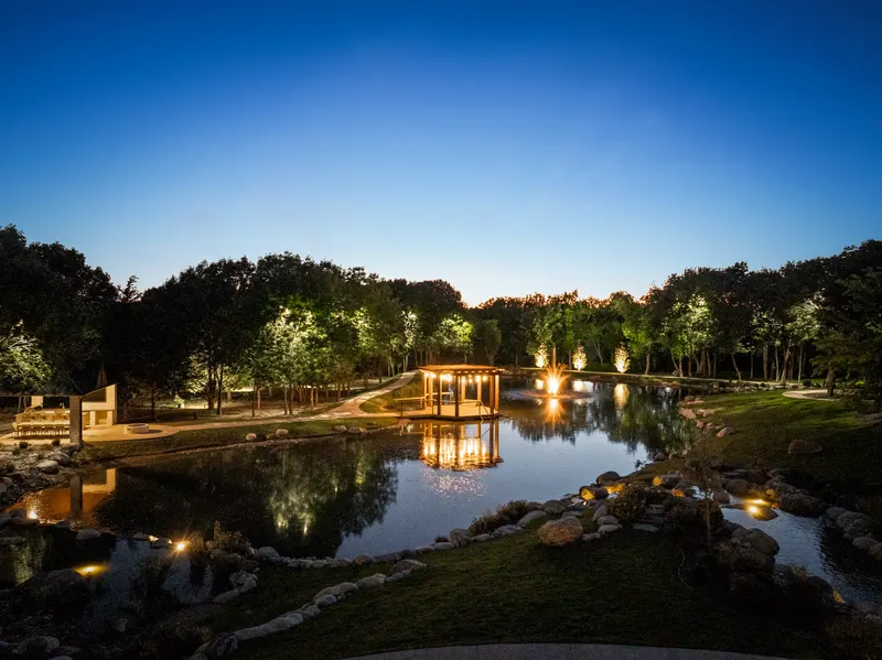 Night aerial over the lit pond, dock pergola and lakeside pavilion at Bella Terra Estate, Parker TX