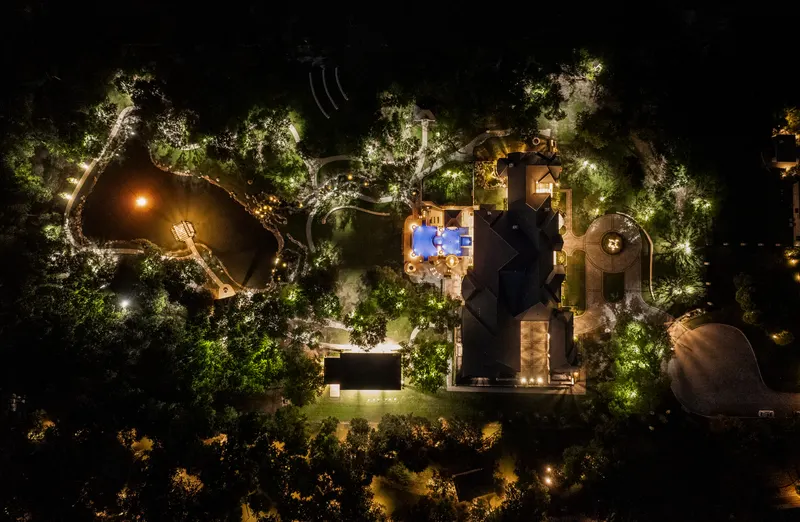 Overhead night aerial showing the house, pool, pond and sport court lit across the grounds