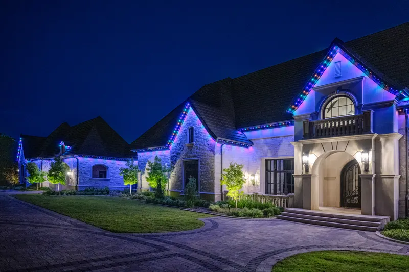 Stone front elevation lit by color-changing roofline lights above the paver drive at Bella Terra Estate, Parker TX