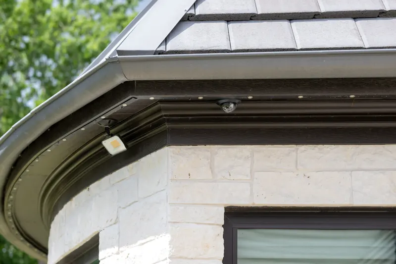 Daytime detail of the roofline LED track and dome security camera on the stone eave at Bella Terra Estate, Parker TX
