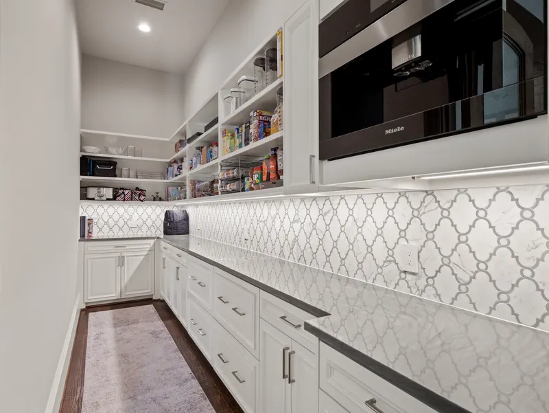 Walk-in pantry with white cabinetry, arabesque marble backsplash and a built-in Miele espresso machine