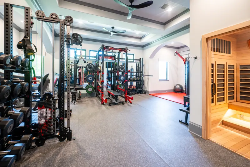 Home gym with power racks, cable machines, dumbbell wall and the infrared sauna beyond the arched doorway