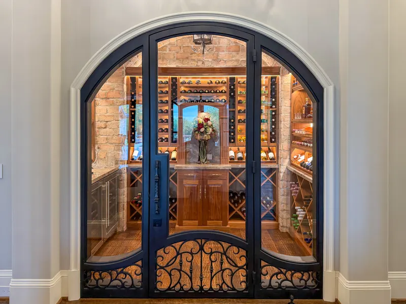 Arched glass and wrought iron doors opening into the brick-vaulted wine room