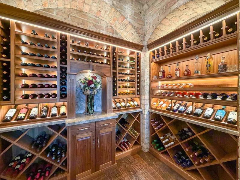 Lit walnut wine racks and spirits display under the reclaimed brick barrel vault